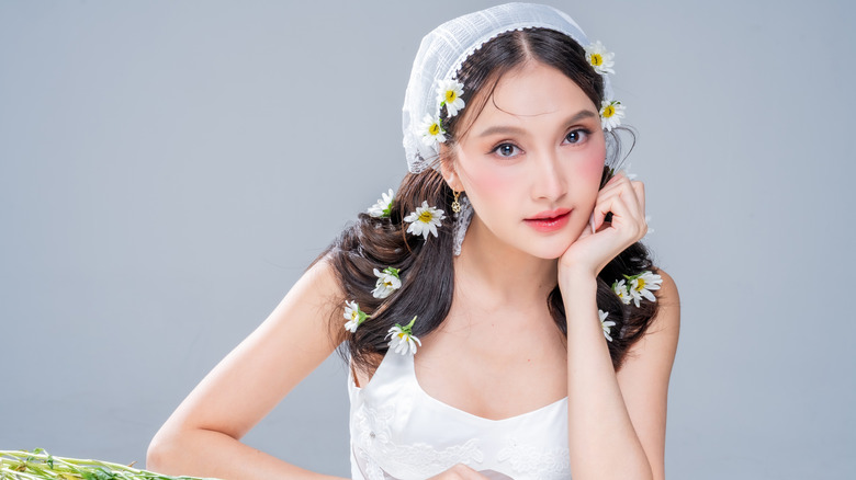 A beautiful woman with cottagecore makeup wearing a scarf with daisies in her hair