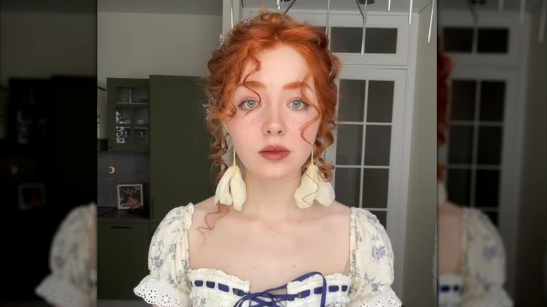 A redhead with cottagecore makeup and flower earrings posing for a photo
