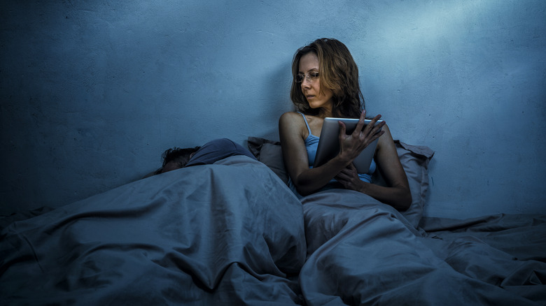 Woman uses social media next to sleeping partner