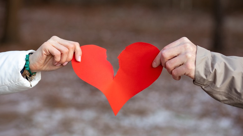 People breaking a paper heart in snow 