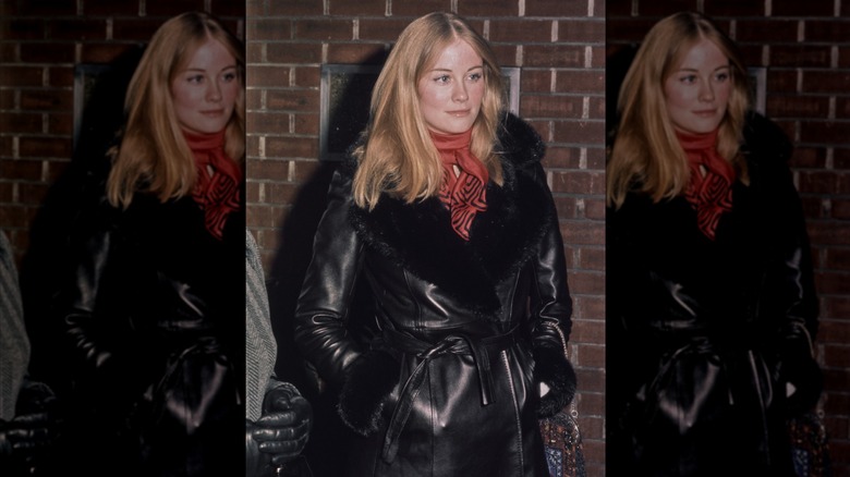 Cybill Shepherd with her hands in her pockets wearing a leather Penny Lane coat and a red neckerchief.