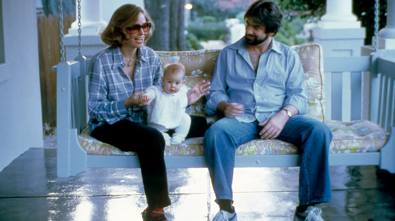 Cybill Shepherd on a porch swing wearing a blue shirt and holding her baby girl next to David M. Ford.