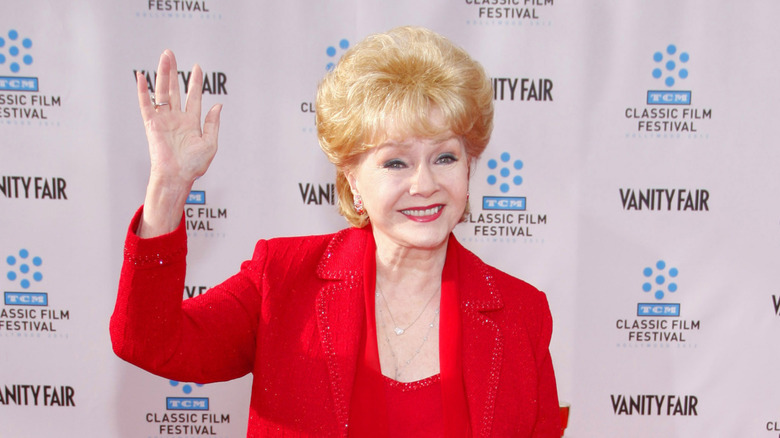 Debbie Reynolds wearing a red outfit waving at an event.