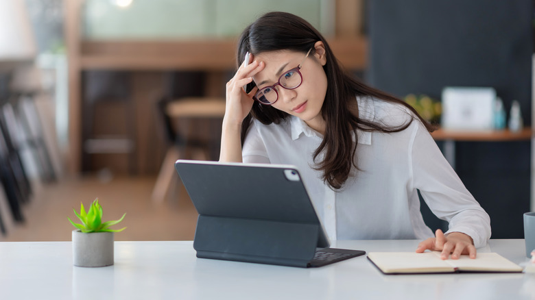 Woman holding head studying iPad