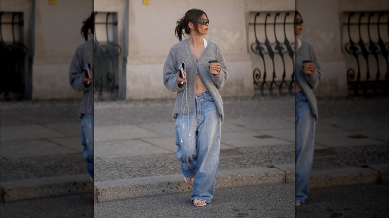 A woman wearing baggy jeans and a partially-buttoned gray cardigan.