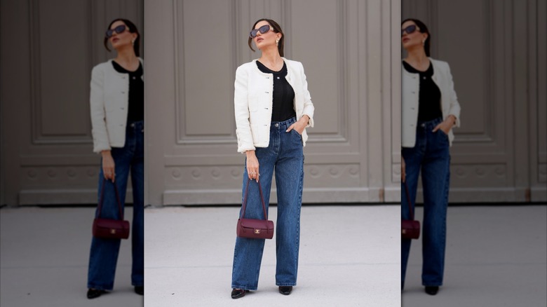 A woman wearing high-waisted jeans, a white jacket, and a black tank top.