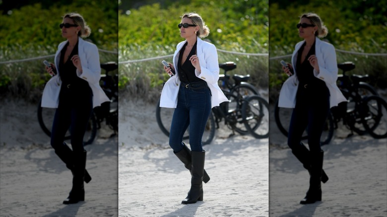A woman wearing skinny jeans, black boots, and a white blazer.