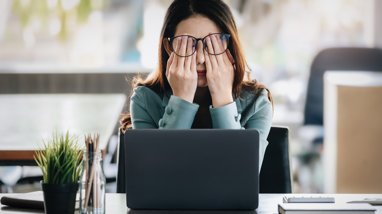 Woman rubbing eyes in front of laptop