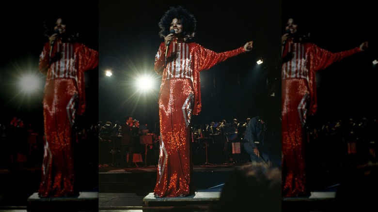 Diana Ross performs on stage wearing a sparkly red and white outfit with a large afro hairstyle.