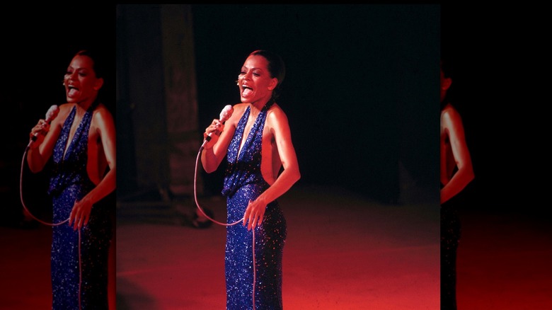 Diana Ross singing into a microphone on stage wearing a sparkly blue dress.