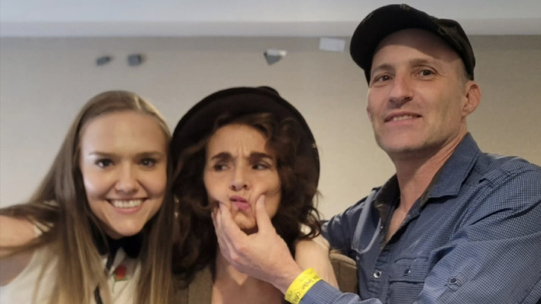 Diane Franklin at a fan convention standing between Dominique Swain and a man who is playfully squeezing her face.