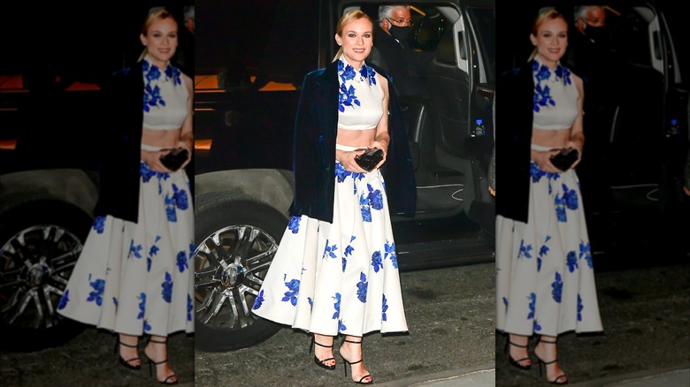 Diane Kruger at an event wearing a white-and-blue floral two-piece crop top and skirt set with a dark blue velvet jacket.