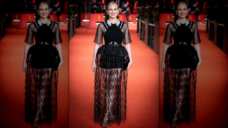 Diane Kruger on the red carpet wearing a black dress with sheer sleeves, and black shorts covered in a long, black lace skirt.