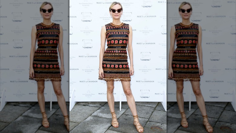 Diane Kruger at an event wearing an intricate stripe pattern mini dress with sunglasses.