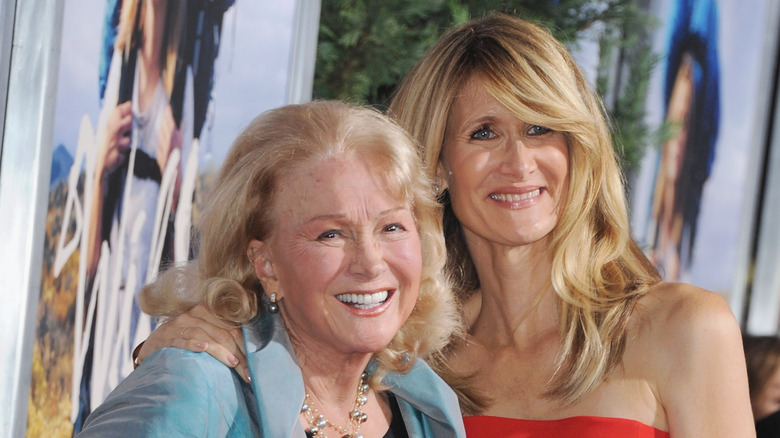 Laura Dern wears a red strapless gown on the red carpet while holding on to the shoulder of her mom Diane Ladd, dressed in a light blue jacket.