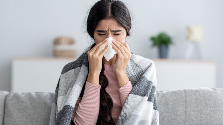 Sick woman blows nose into tissue