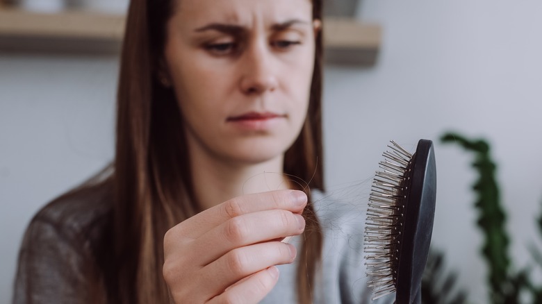 Woman looking at hair on hairbrush with worried expression