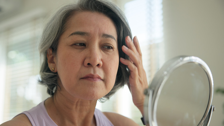Mature woman with graying hair looks into a small round mirror