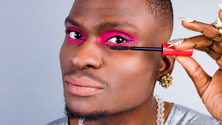 Man applying mascara with neon pink eyeshadow look