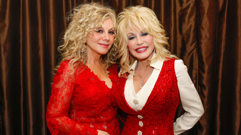 Stella Parton and Dolly Parton pose together in matching sparkly red outfits.