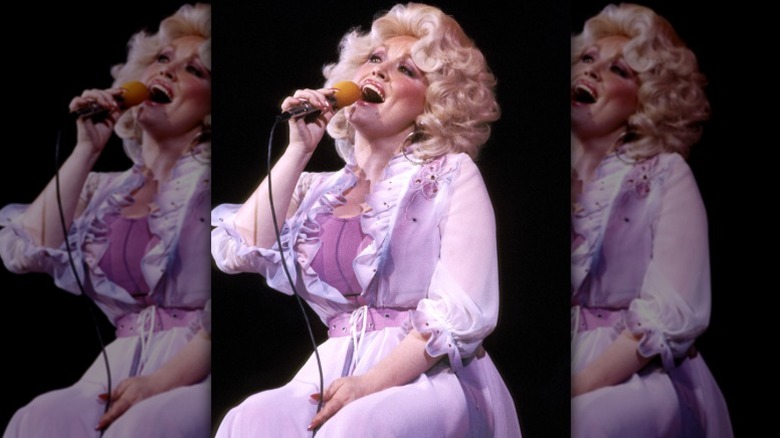 Dolly Parton sings into a microphone as she performs for an audience