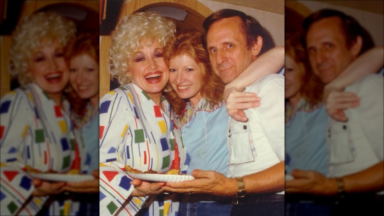 Dolly Parton (left) embraces Judy Ogle (middle) who wears a light blue top and a ginger bob