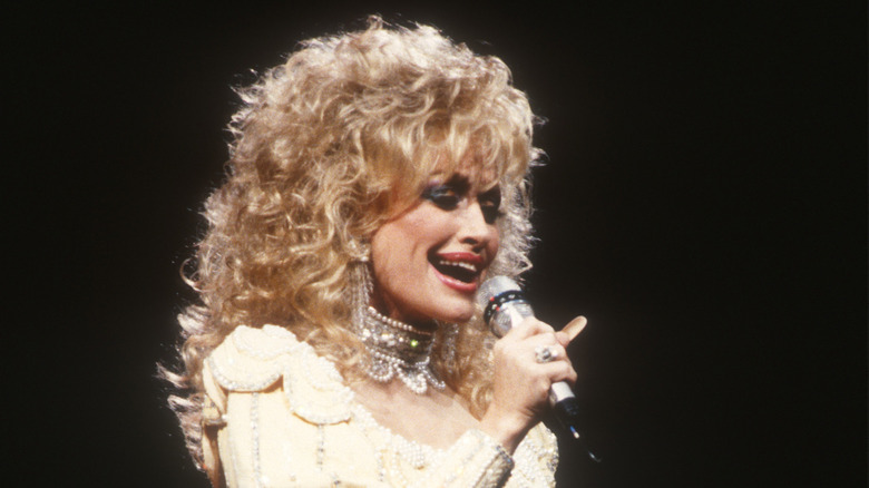 Dolly Parton sings into a microphone with curly blond hair