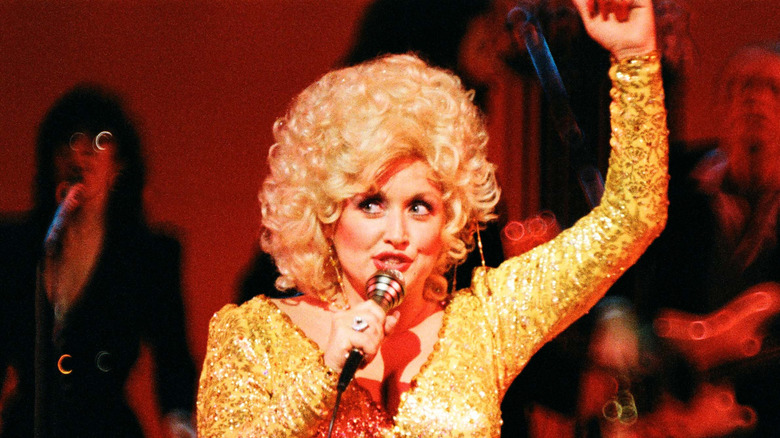 Dolly Parton wearing a perm-inspired wig and a gold jumpsuit