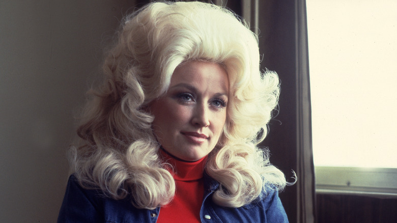 Dolly Parton wearing a voluminous blond wig, a red turtleneck, and a blue shirt