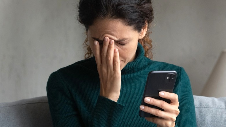 Woman rubbing forehead while looking at phone