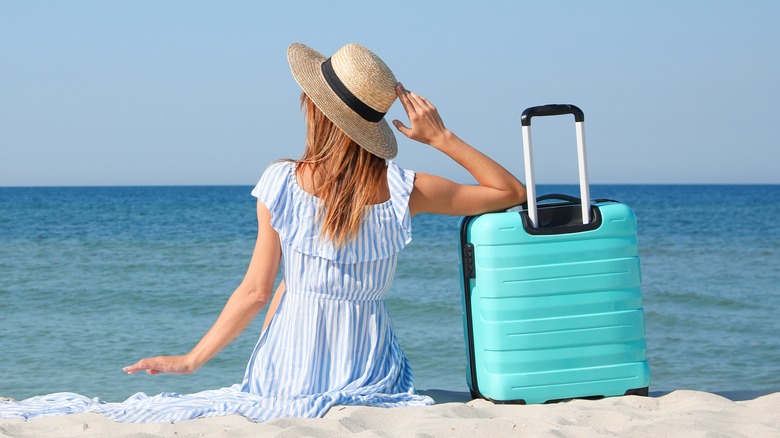 Woman sitting on beach with luggage