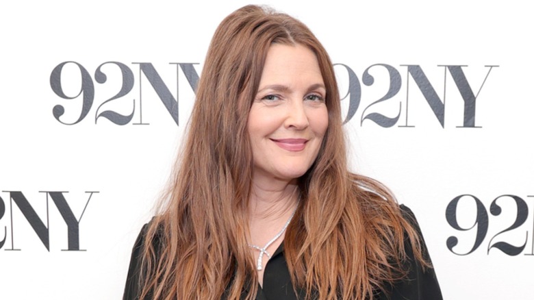 Drew Barrymore posing at a red carpet event wearing black.