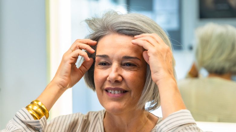 Mature woman smiling and fixing her hair with a mirror behind her.