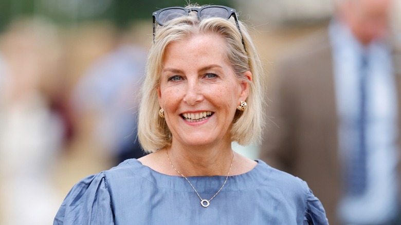 Duchess Sophie smiling outside with sunglasses on top of her head wearing a blue top with a bob haircut.