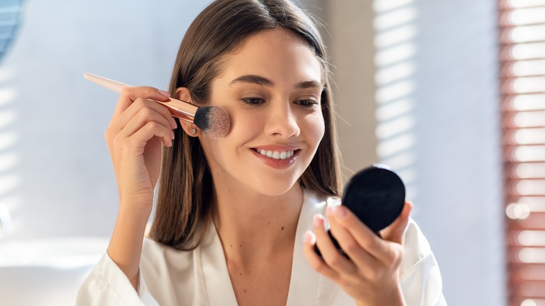 Woman smiling as she applies makeup