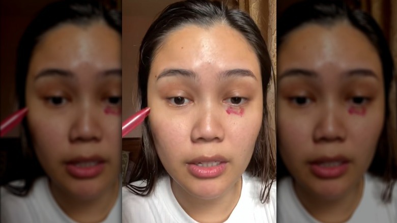 Woman applying red lipstick under eye as color corrector
