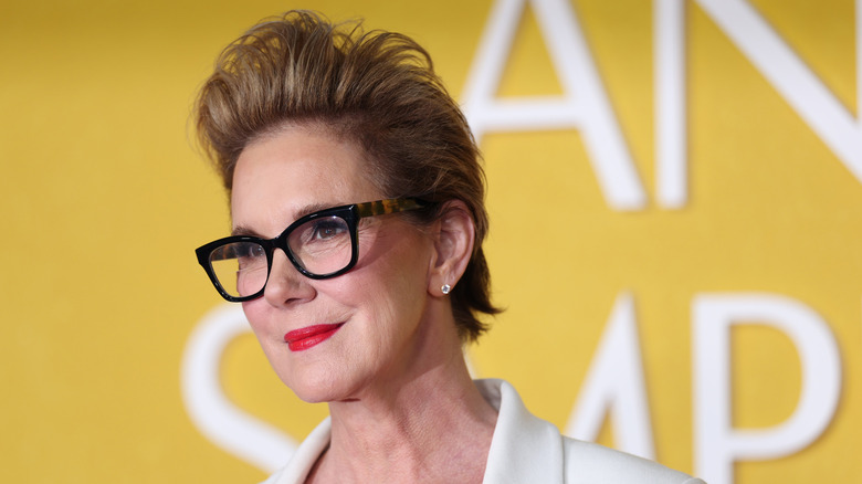 Elizabeth  Perking smiles for a photo wearing glasses and red lipstick as she walks the carpet at an event