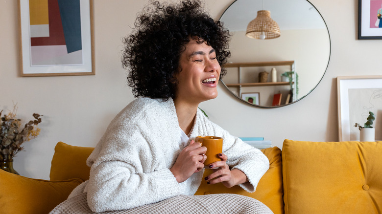 Model laughing on sofa with mug and blanket