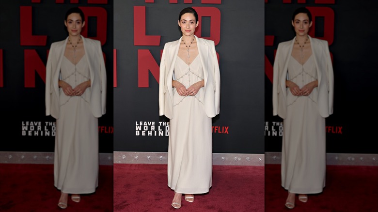 Emmy Rossum wears a white blazer and dress with a long silver body chain