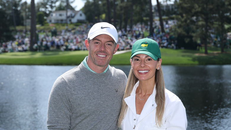 Erica Stoll and Rory McIlroy smile in front of a golf course with a large pond