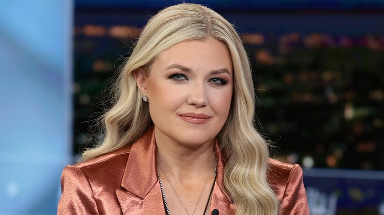 An image of Erika Kirk being interviewed. Kirk is a young white woman with long blonde hair. She is wearing a full face of heavy makeup, as well as a rose gold metallic blazer.