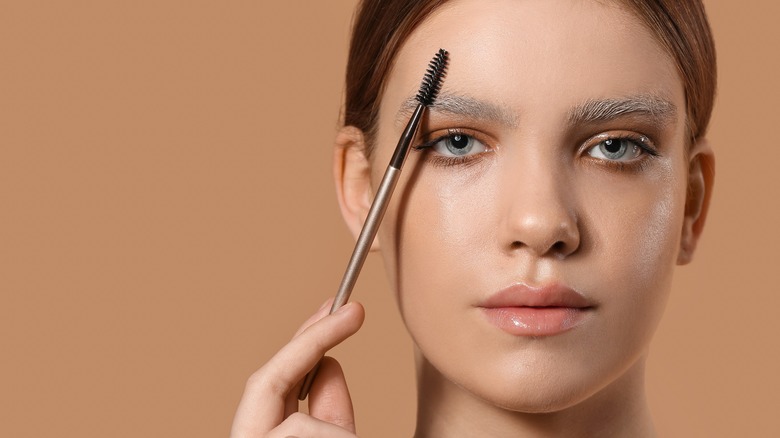 Woman with bleached eyebrows holding a brow brush