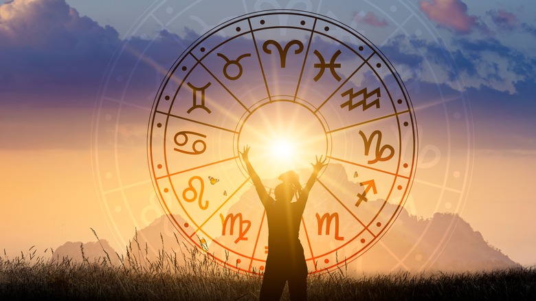 Zodiac wheel imposed over woman reaching for the sun
