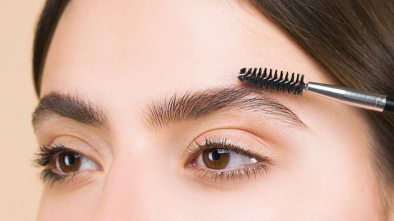 woman brushing eyebrows with spoolie