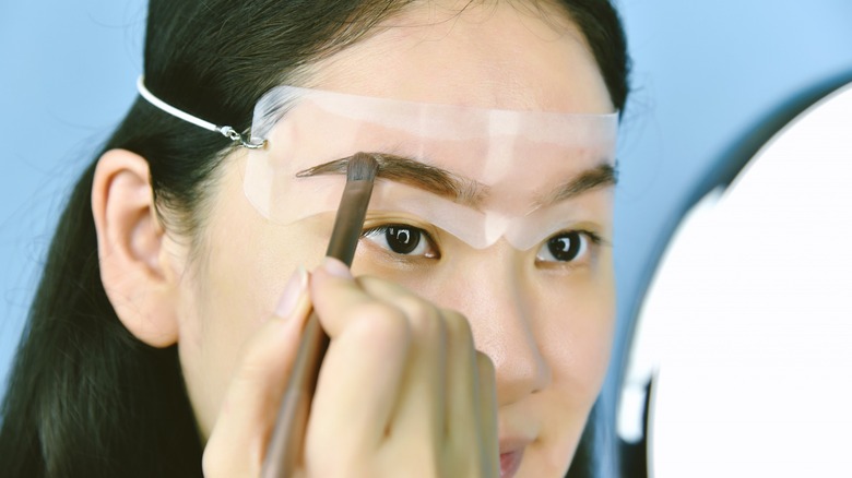 Woman applying makeup with eyebrow stencil