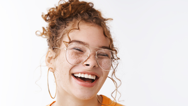 Woman smiling wearing hair in bun with curly tendrils 