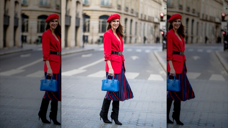 A woman wearing a red blazer, black belt, and a blue and red striped skirt.