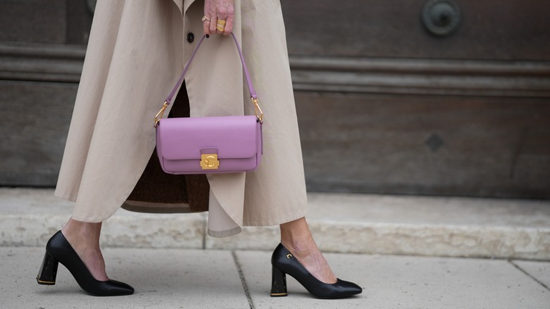 A cropped photo of a woman carrying a purple purse and wearing black heels
