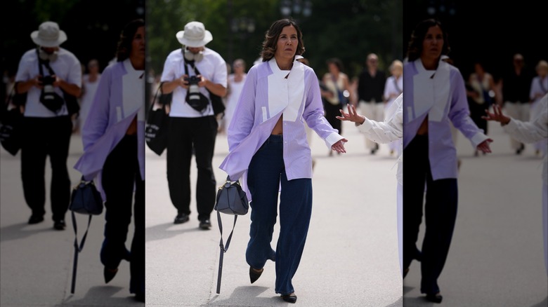 A woman wears dark wash jeans and a light purple and white button-down shirt.