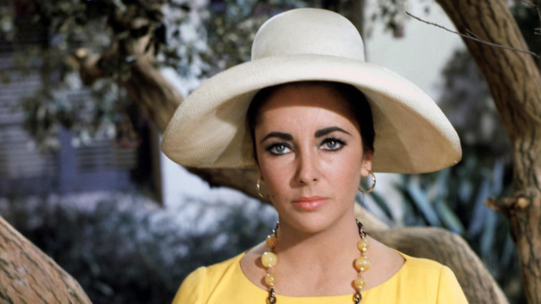 Elizabeth Taylor posing in a large hat and yellow outfit